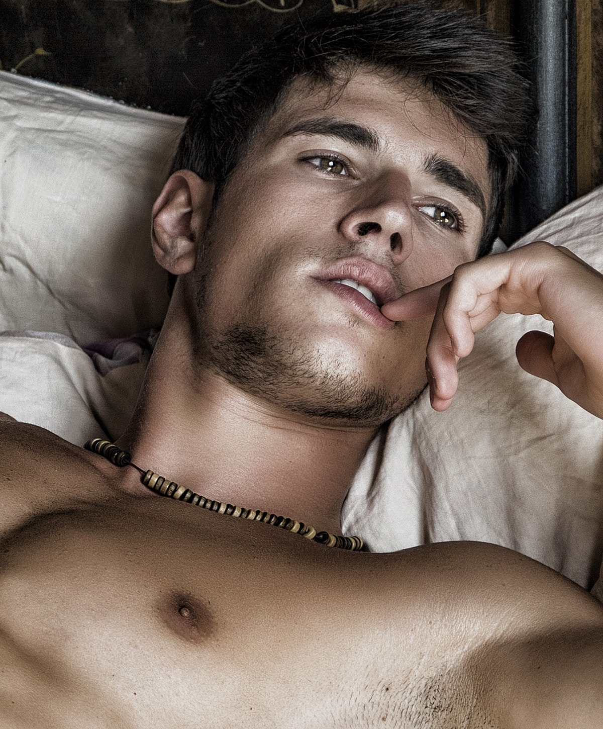 Young man reclining on bed, deep in thought.